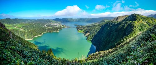 A mesmerizing view of the lake surrounded by mountains covered in green under the blue sky